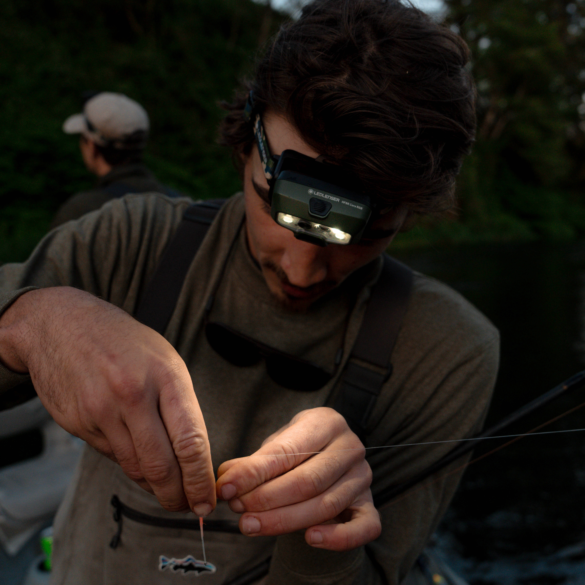 HF8R Core RGB Camo headlamp worn on the head by a person in a dim outdoor fishing setting with dual LEDs visible