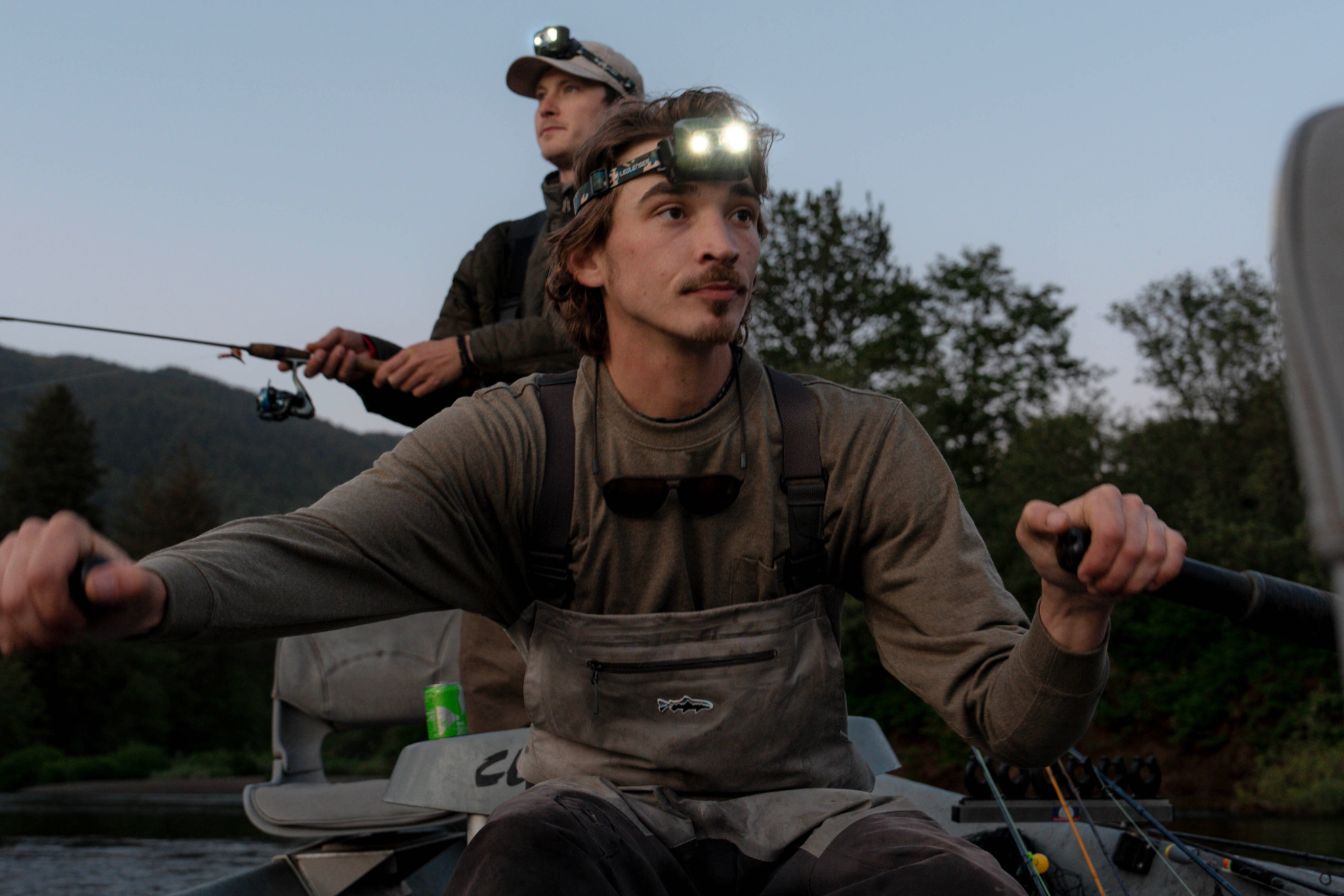 HF8R Core RGB Camo headlamp worn by a man in a boat while fishing at dusk camo headband with another person in the background
