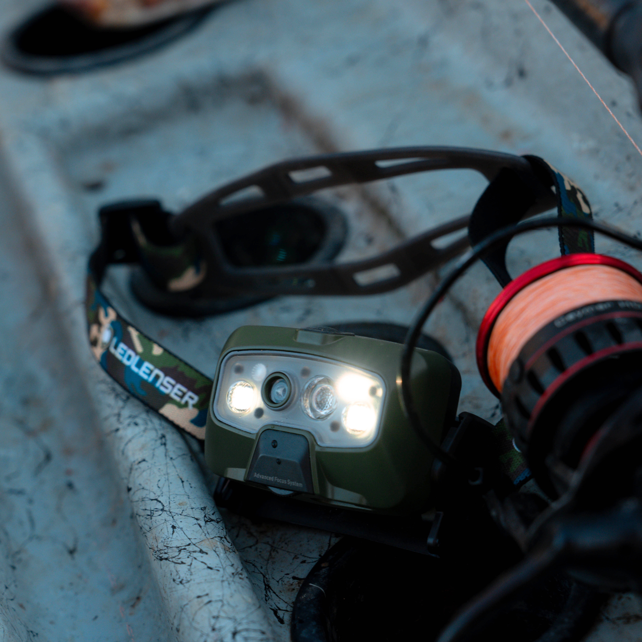 Ledlenser HF8R Core RGB Camo headlamp in olive green with dual front LEDs on a camo adjustable headband and a charging cable nearby