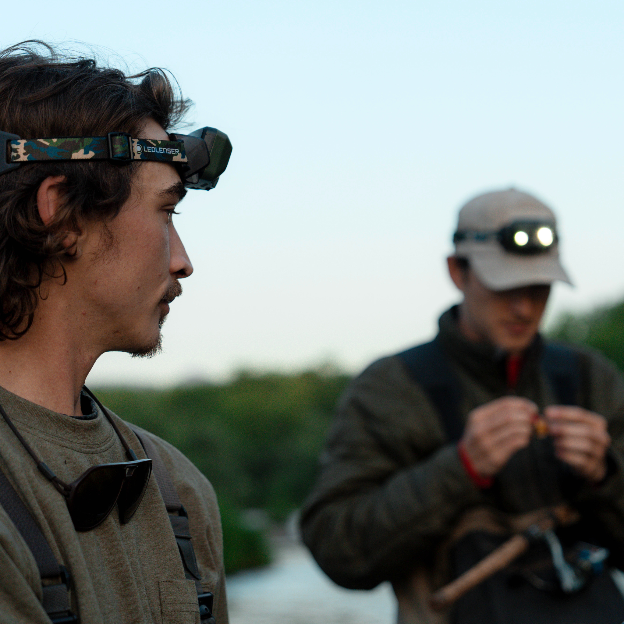 HF8R Core RGB Camo headlamp worn by a person with a camouflage headband in foreground with another lit headlamp in the background