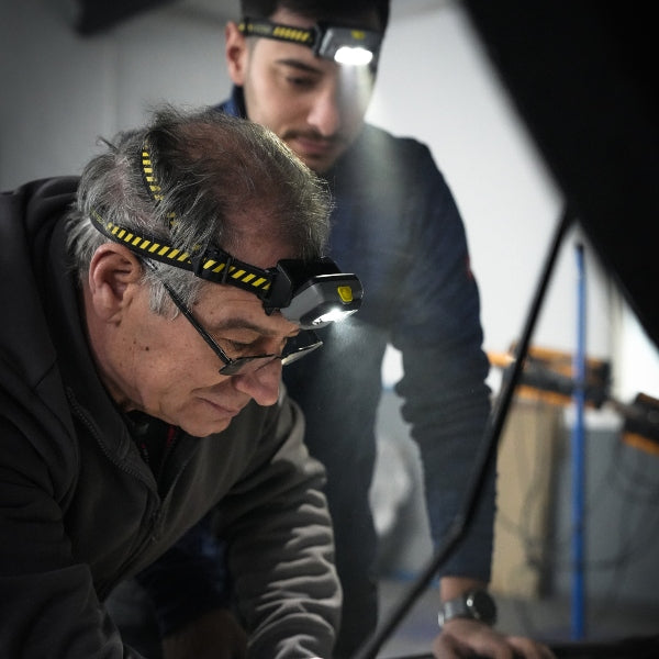 HF4R Work Headlamp in use on two workers; foreground man wears black headlamp with yellow striped strap and bright light