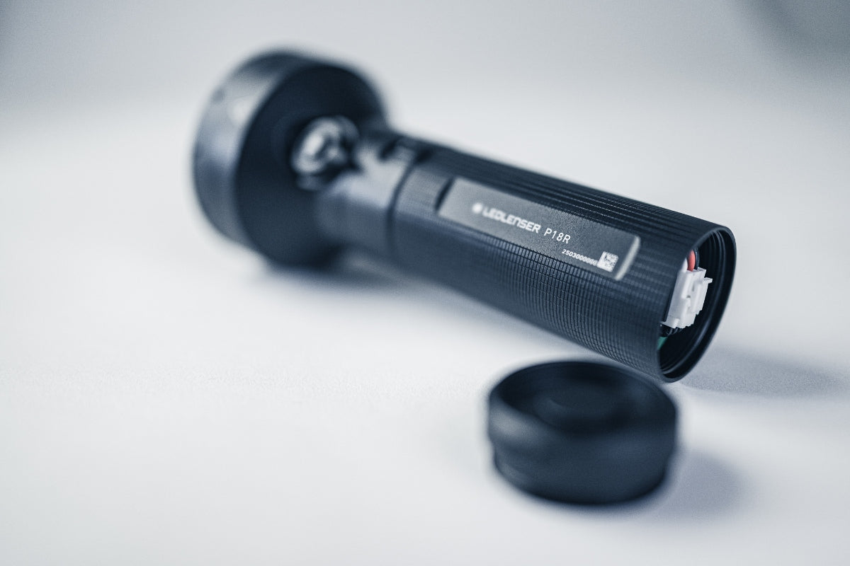 Ledlenser P18R Torch lying on its side with end cap removed exposing the internal connector and textured black body