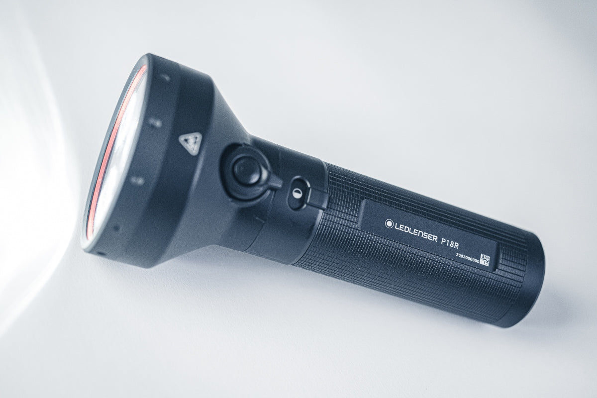 Ledlenser P18R torch in a side angle view black textured body with red ring bezel at the front and visible product label on the side