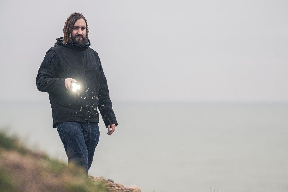 Ledlenser P18R Torch held by a man outdoors near a lake wearing a dark jacket in use with the torch visible