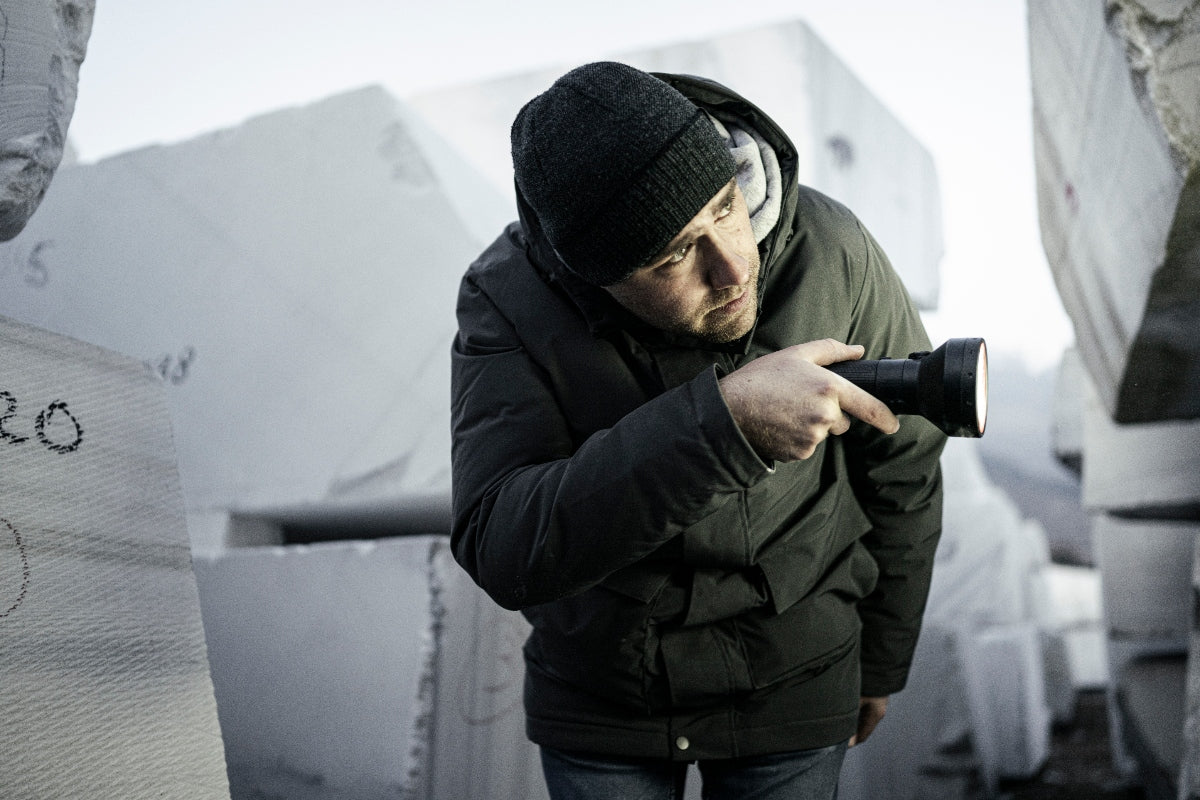 Person wearing a black beanie and jacket holds a Ledlenser P18R Torch pointed outward in a cold outdoor setting among large ice blocks