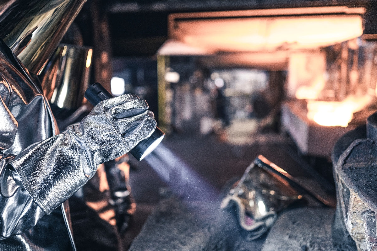 Ledlenser P18R Torch held in a gloved hand illuminating an industrial workshop with a blue beam in a foundry setting