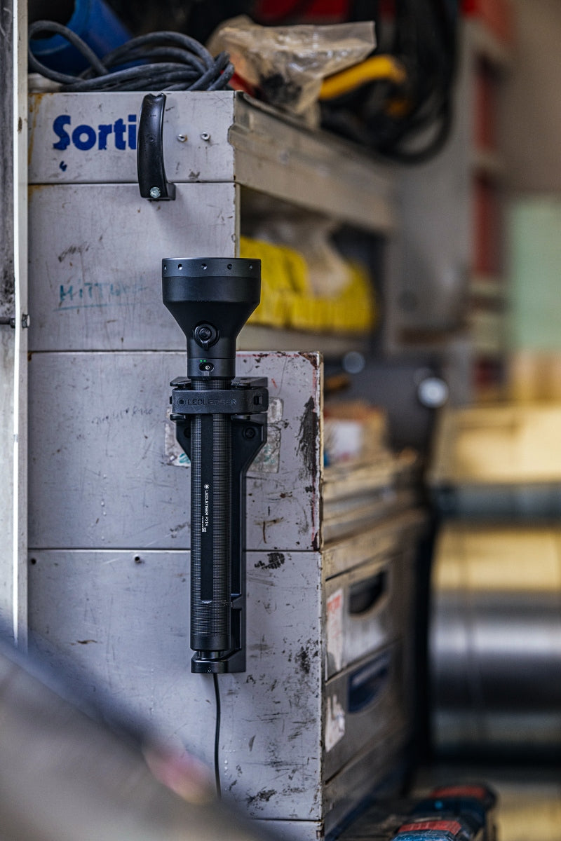 Ledlenser P21R torch mounted vertically on a metal cabinet in a workshop black finish with charging cable visible