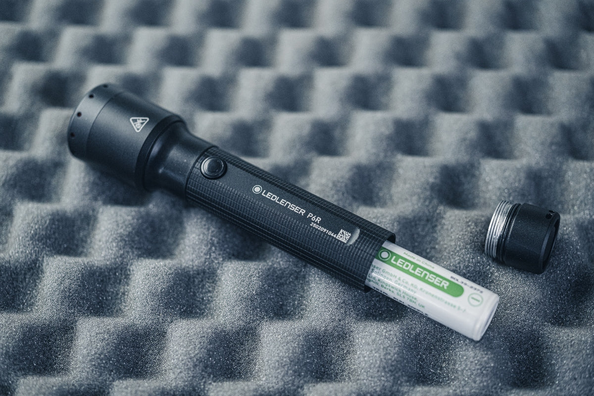 P6R Torch lying on foam backdrop with battery and cap nearby; a black Ledlenser torch with textured grip and side button