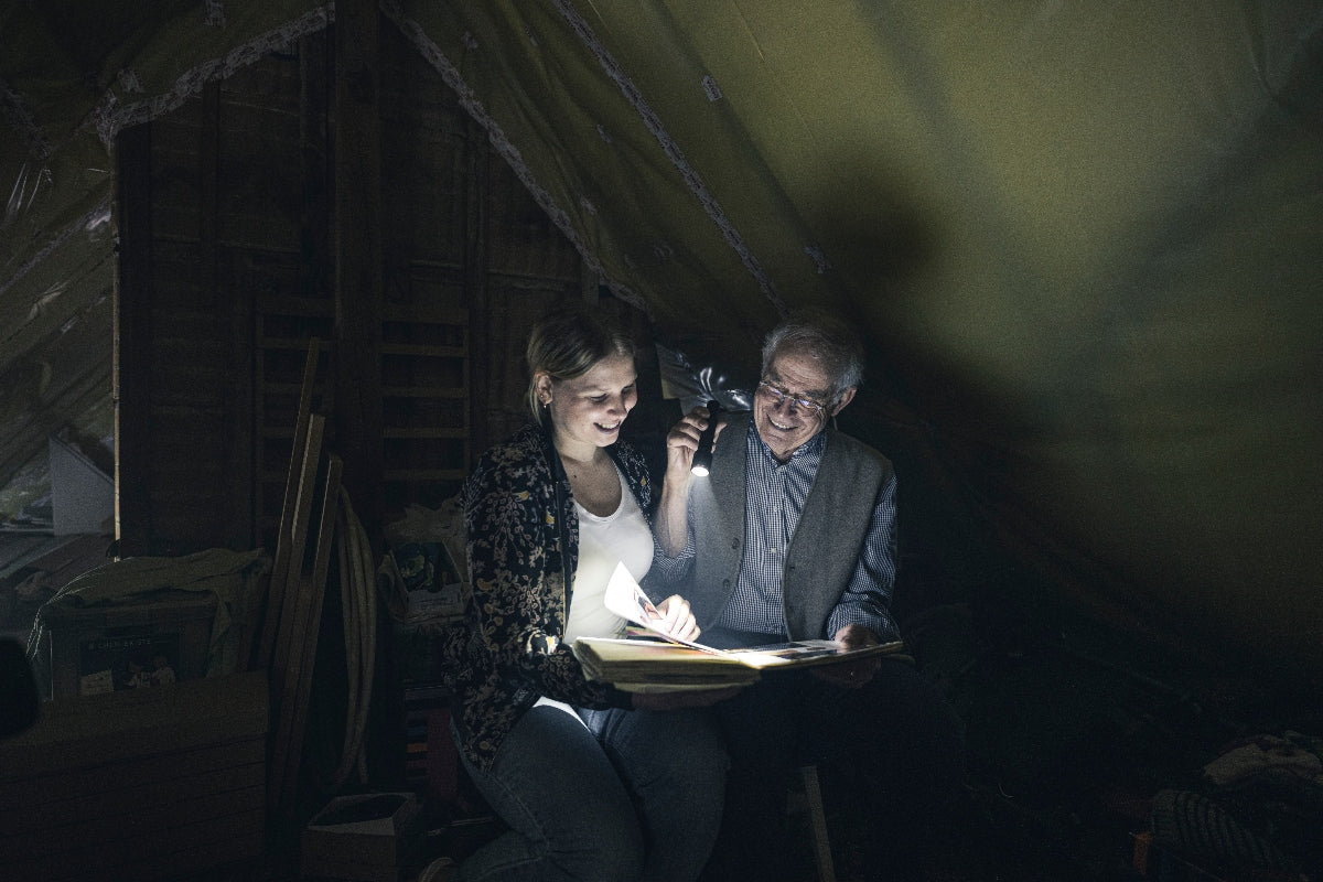 Ledlenser P6R Torch held by a man in a dark attic as he illuminates a book with a woman nearby