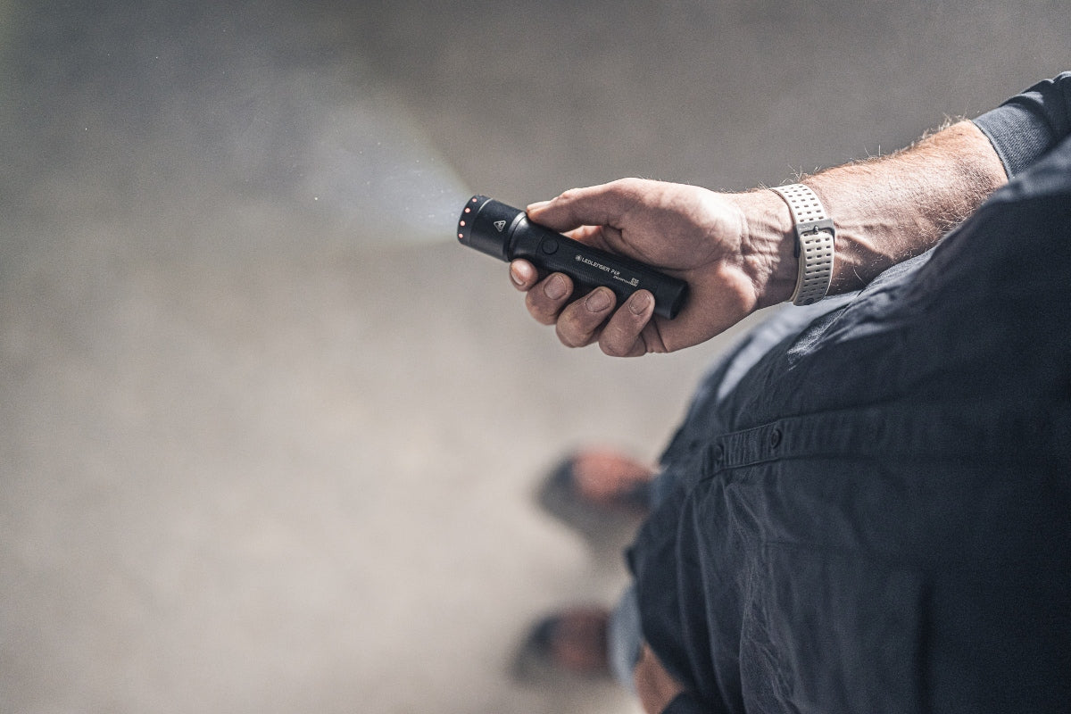 P6R Torch held in a right hand beam forward in a dark outdoor setting; compact black rechargeable flashlight with Ledlenser branding visible