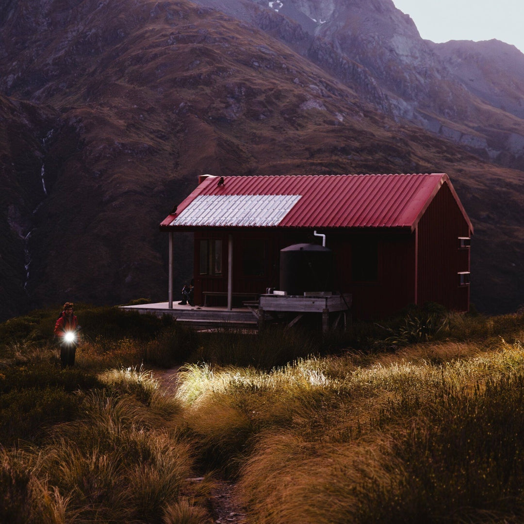 Ledlenser P7R Signature Torch held by a person illuminating a path near a red mountain cabin at dusk