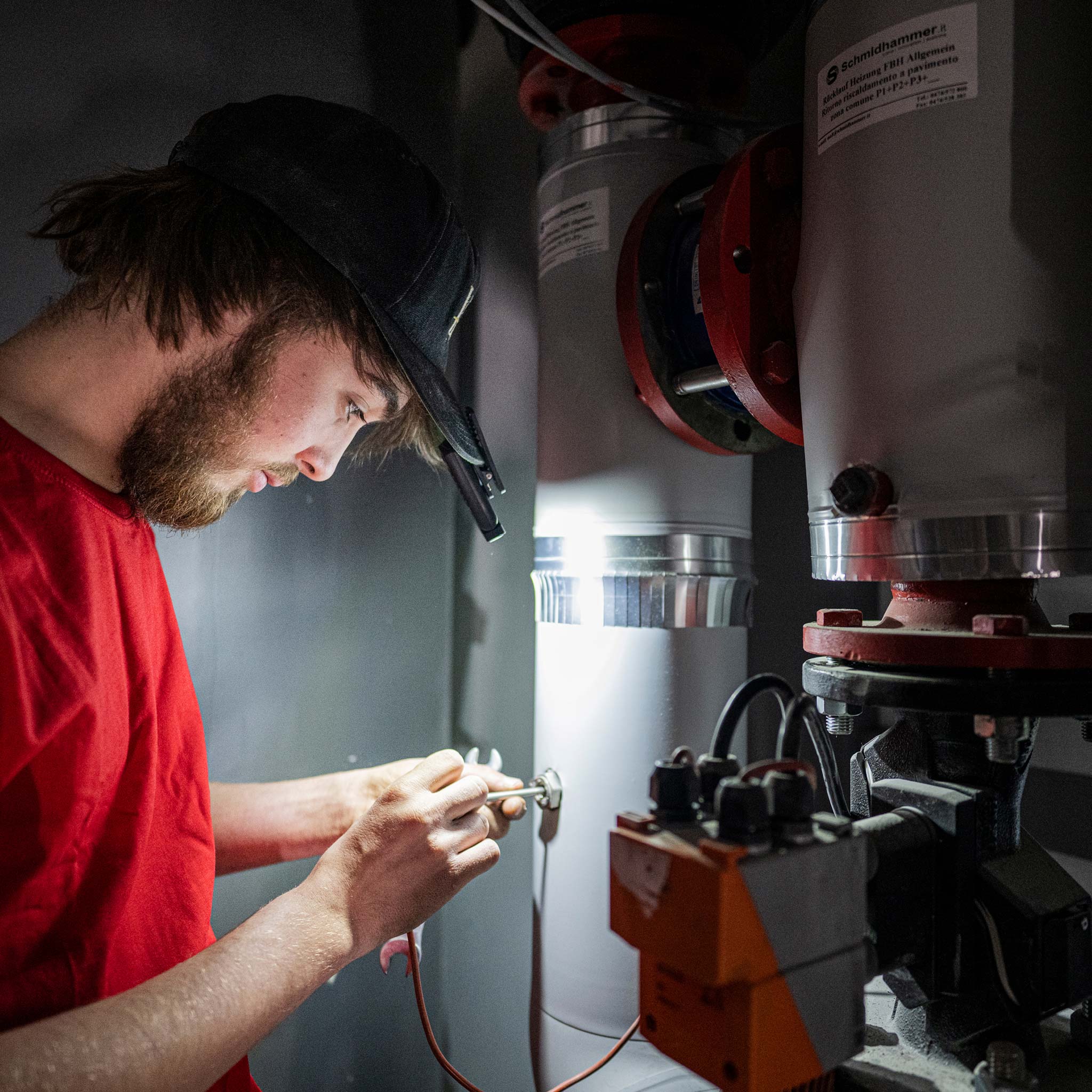 Ledlenser W1R Work Clip Light worn on a cap lighting a technician working on industrial pipe fittings in a workshop environment