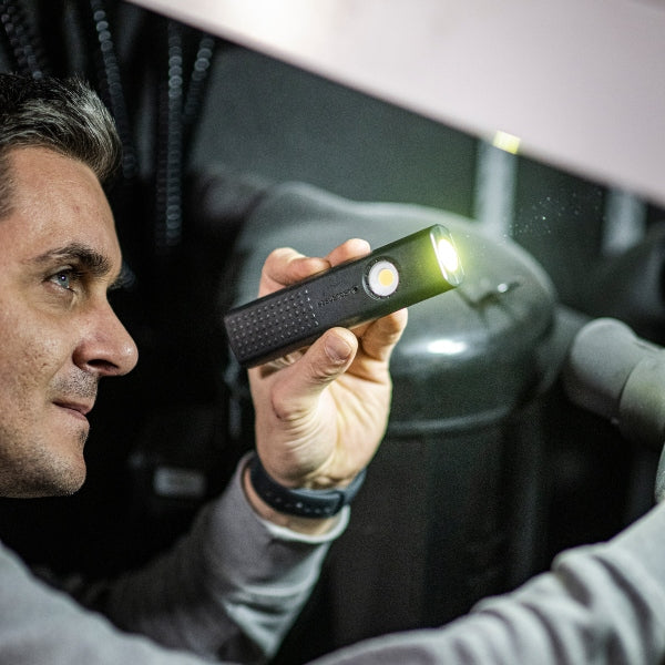 Ledlenser W5R Work Light held by a man in a dim workshop a compact black handheld light with front LED illuminated