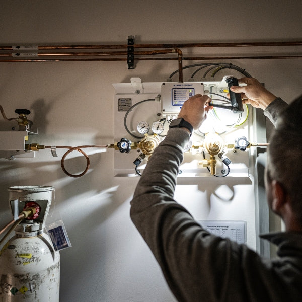 W7R Work Light being adjusted by a technician inside a utility panel area with gauges and copper piping