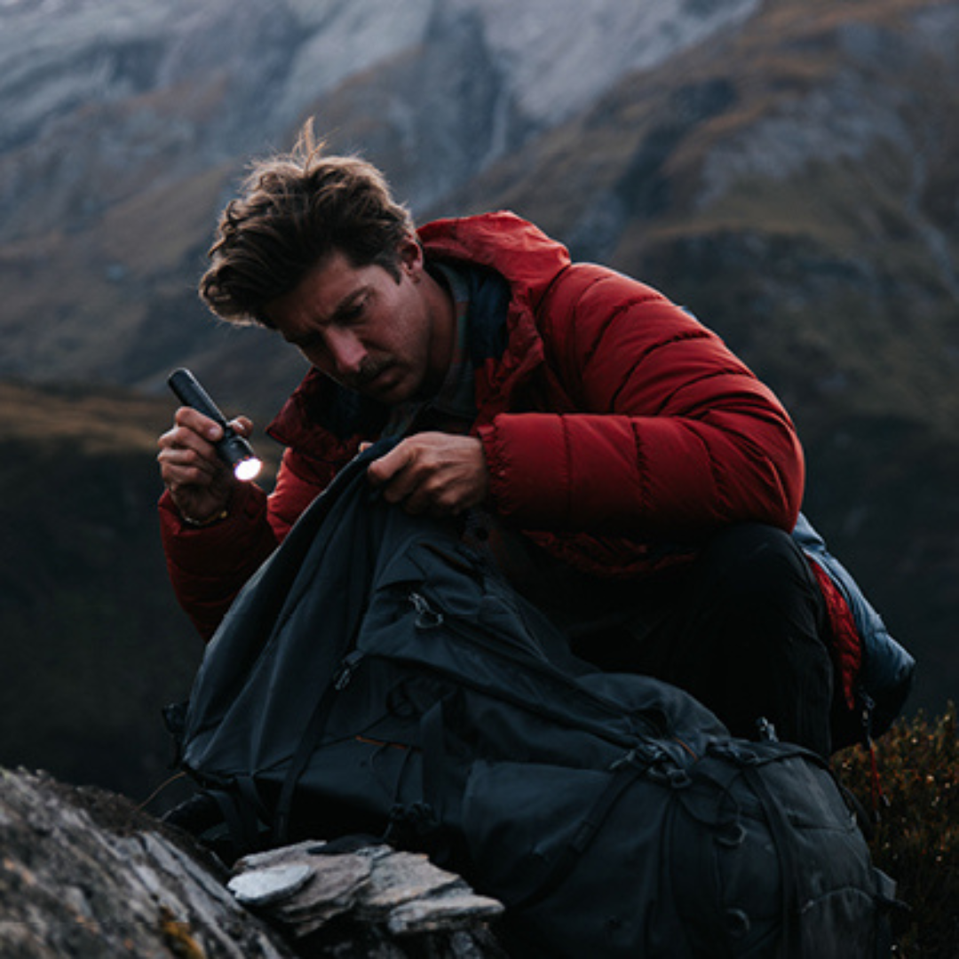 Ledlenser P7R Signature Torch handheld by a man in a red outdoor jacket on rocky terrain at dusk