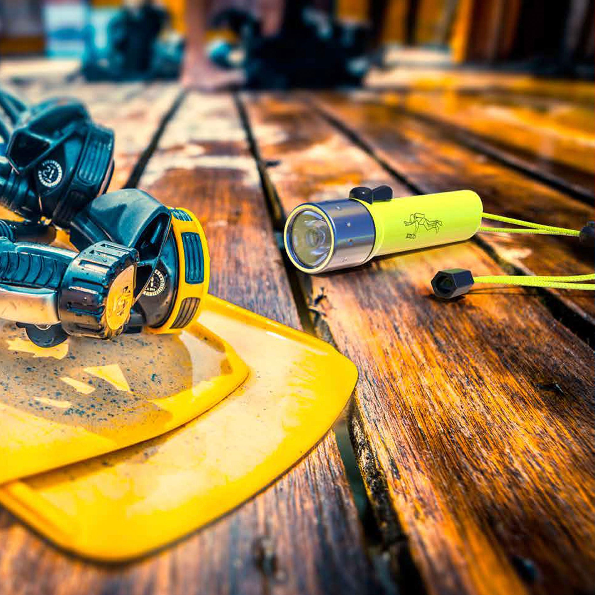 D14 2 Battery Operated Torch yellow green compact flashlight with silver bezel on a wooden workbench beside a yellow safety helmet