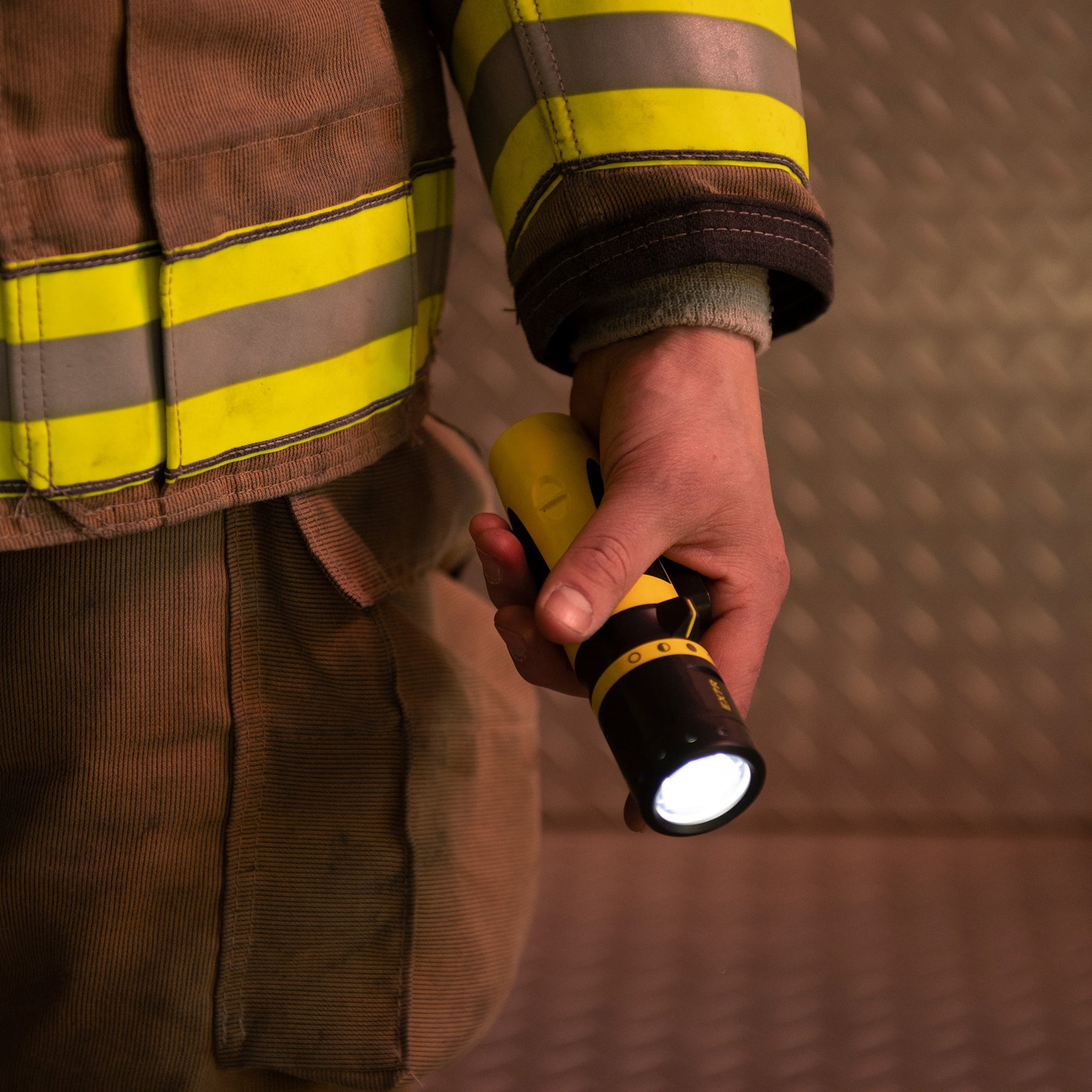 Ledlenser EX7R Torch held in a worker's hand beside a high visibility jacket; yellow and black compact rechargeable flashlight