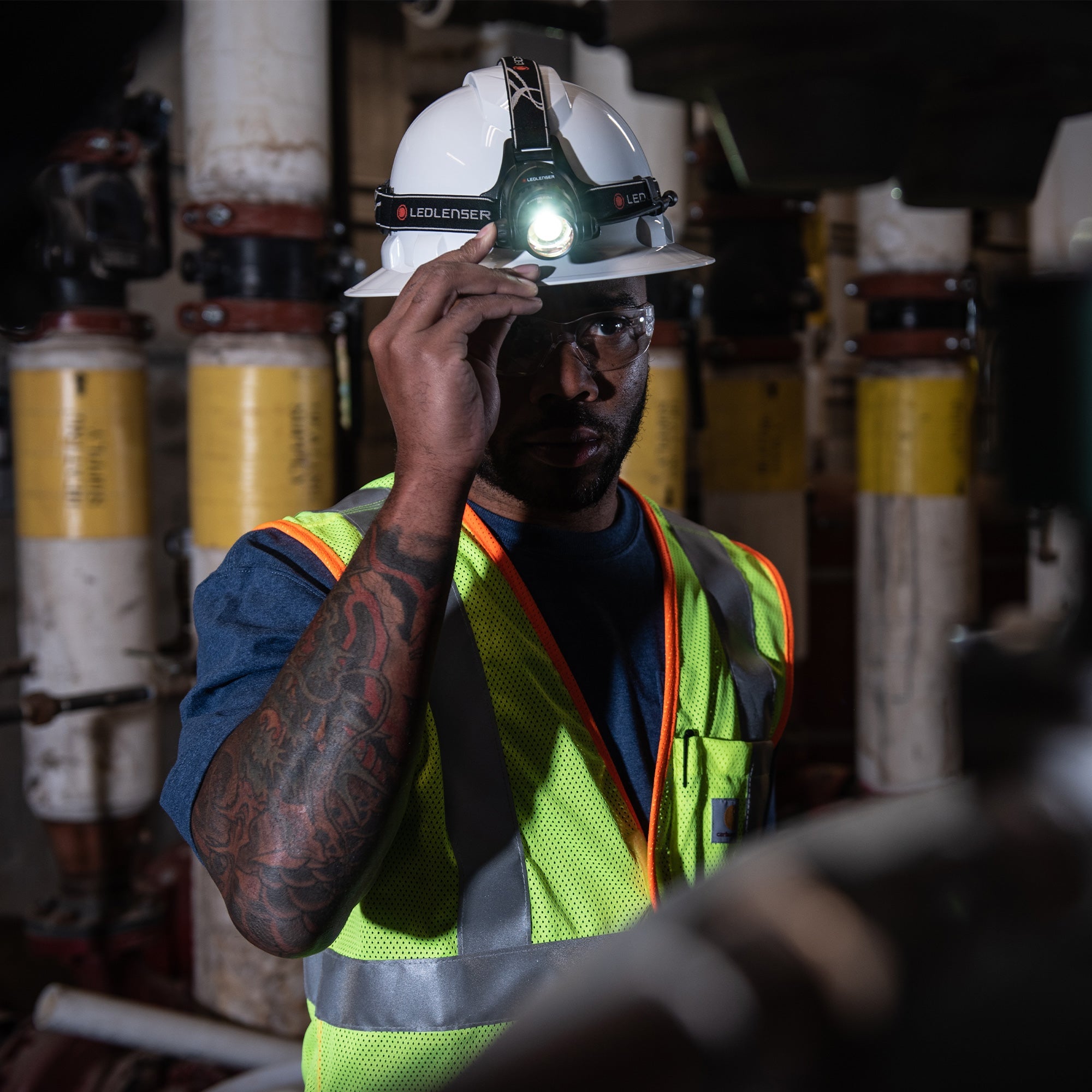 Ledlenser H14R 2 Headlamp worn on a white safety helmet by a worker in an industrial setting with the light on