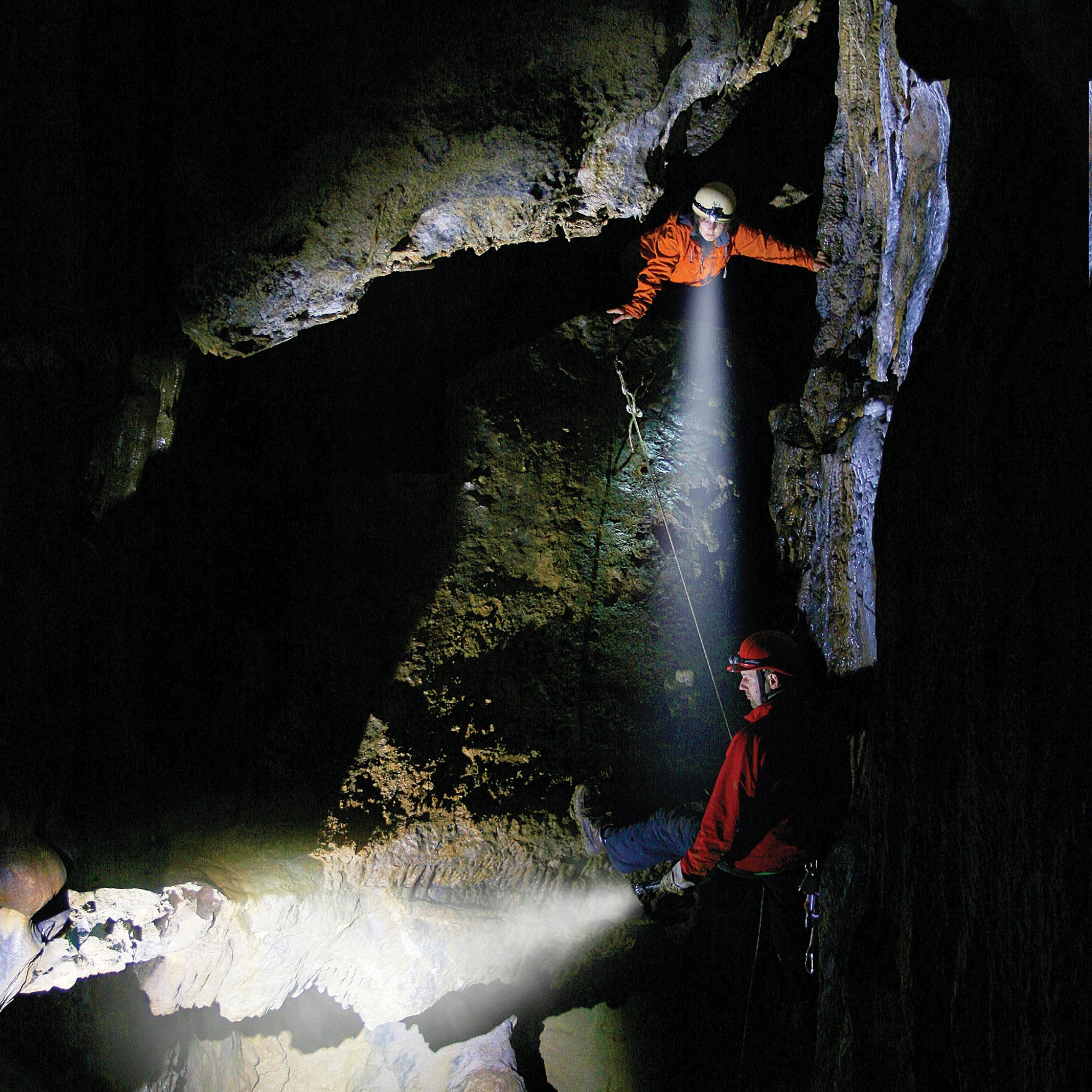Ledlenser H3 2 Battery Operated Headlamp in use by two cavers in a dark cave orange and red jackets with a bright beam emerging from the headlamp