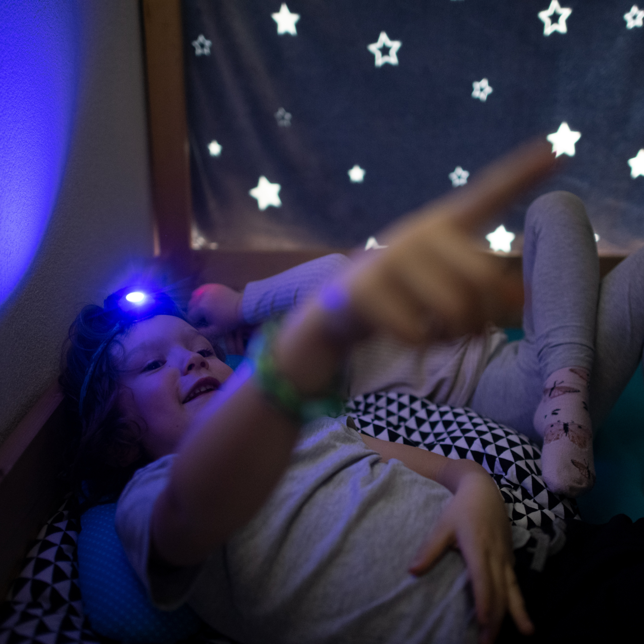 Ledlenser Kidled2 Headlamp worn by a child lying down blue light visible on the head strap against a starry backdrop