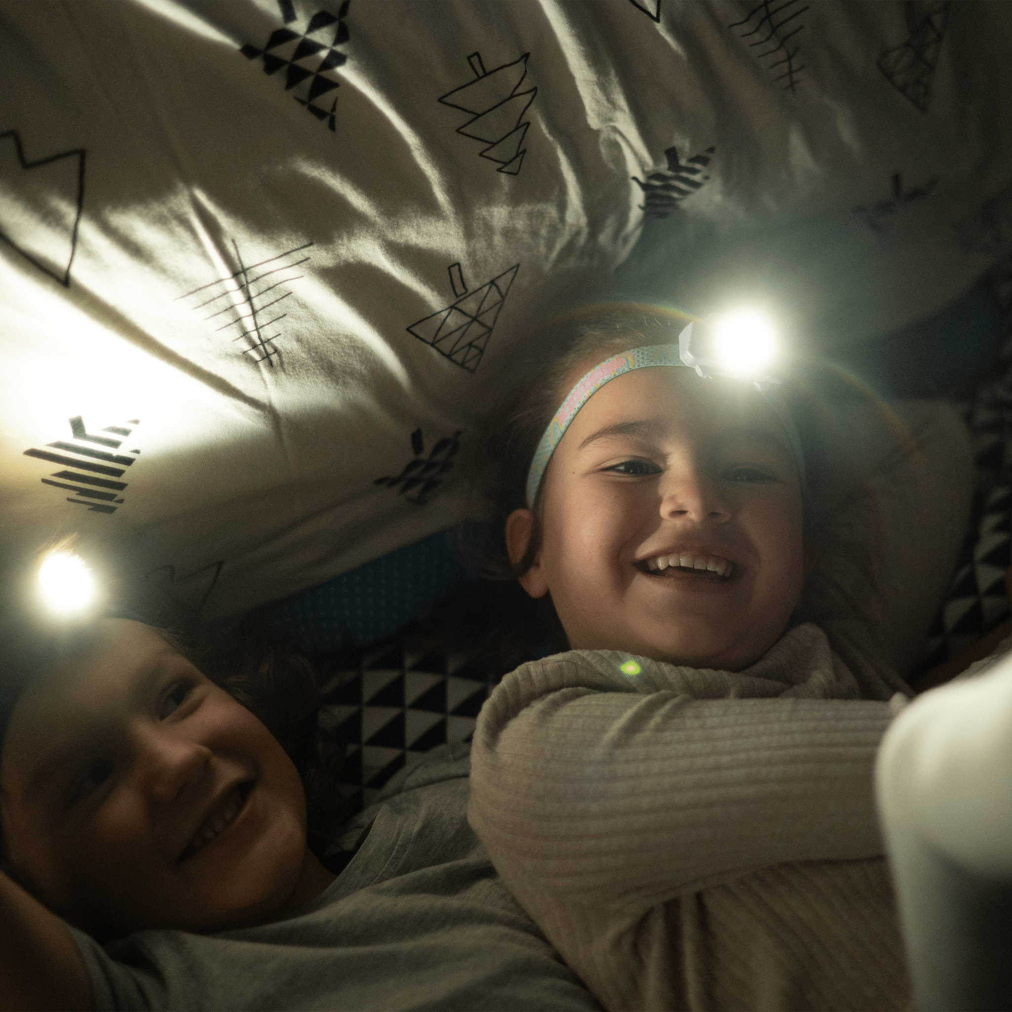 Kidled4R Headlamp worn by a smiling child with a light on the headband in a cozy indoor setting beam visible