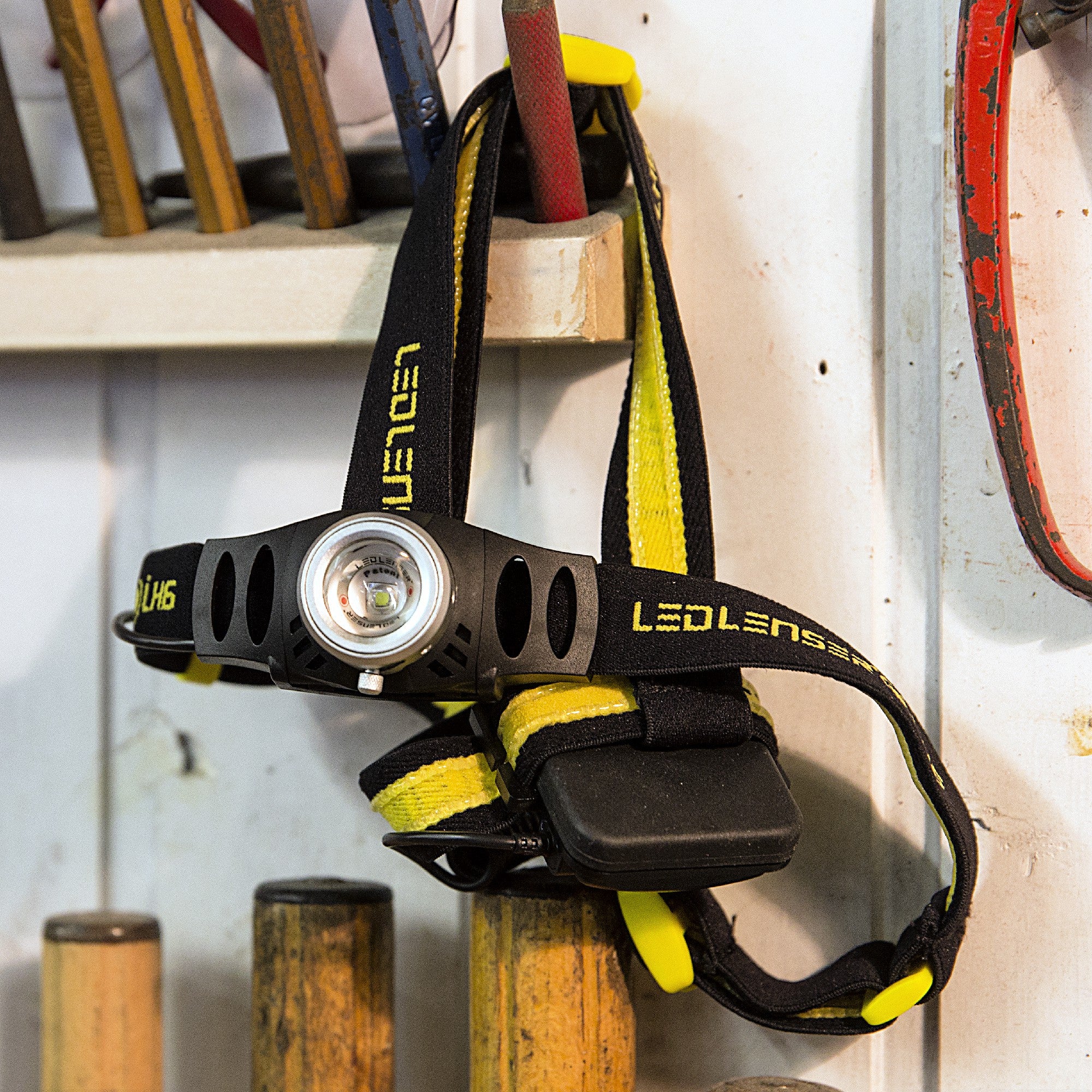 iH6R Rechargeable Headlamp mounted on its black yellow strap with the Ledlenser logo shown on a workbench with tools
