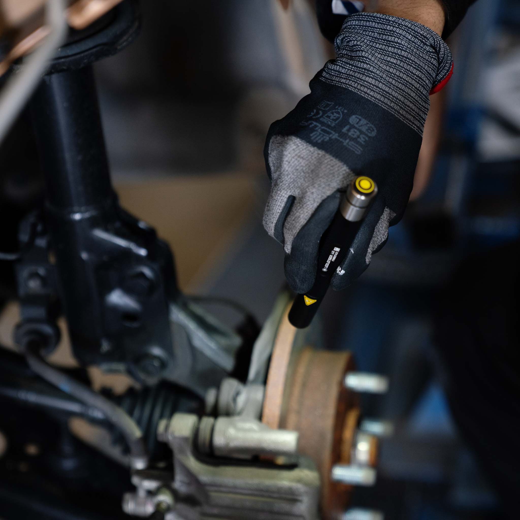 Ledlenser i4 Torch held in gloved hand above industrial machinery with yellow activation button visible