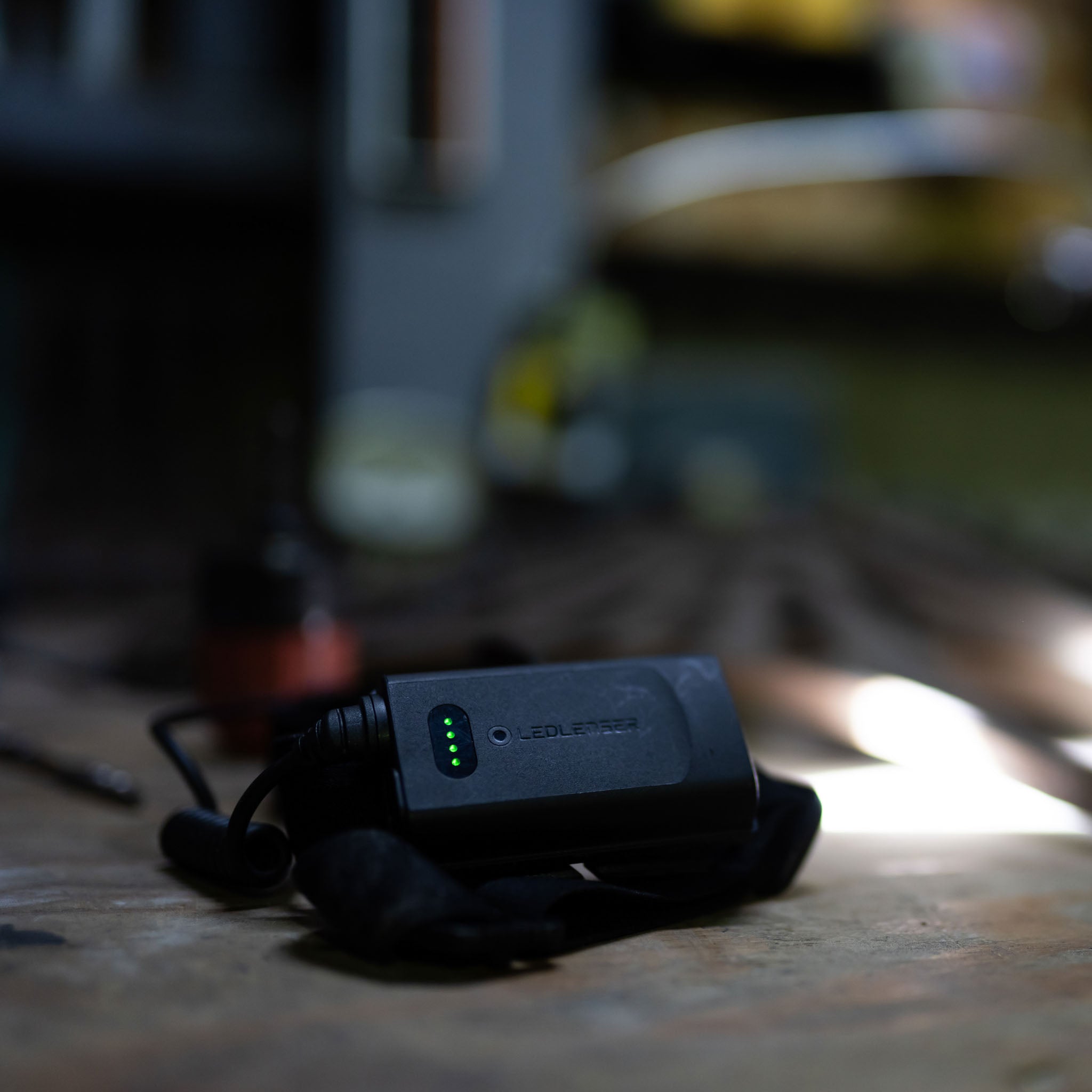 Ledlenser H15R Core Headlamp charging unit with green indicator LEDs on a workbench in a dim workshop setting