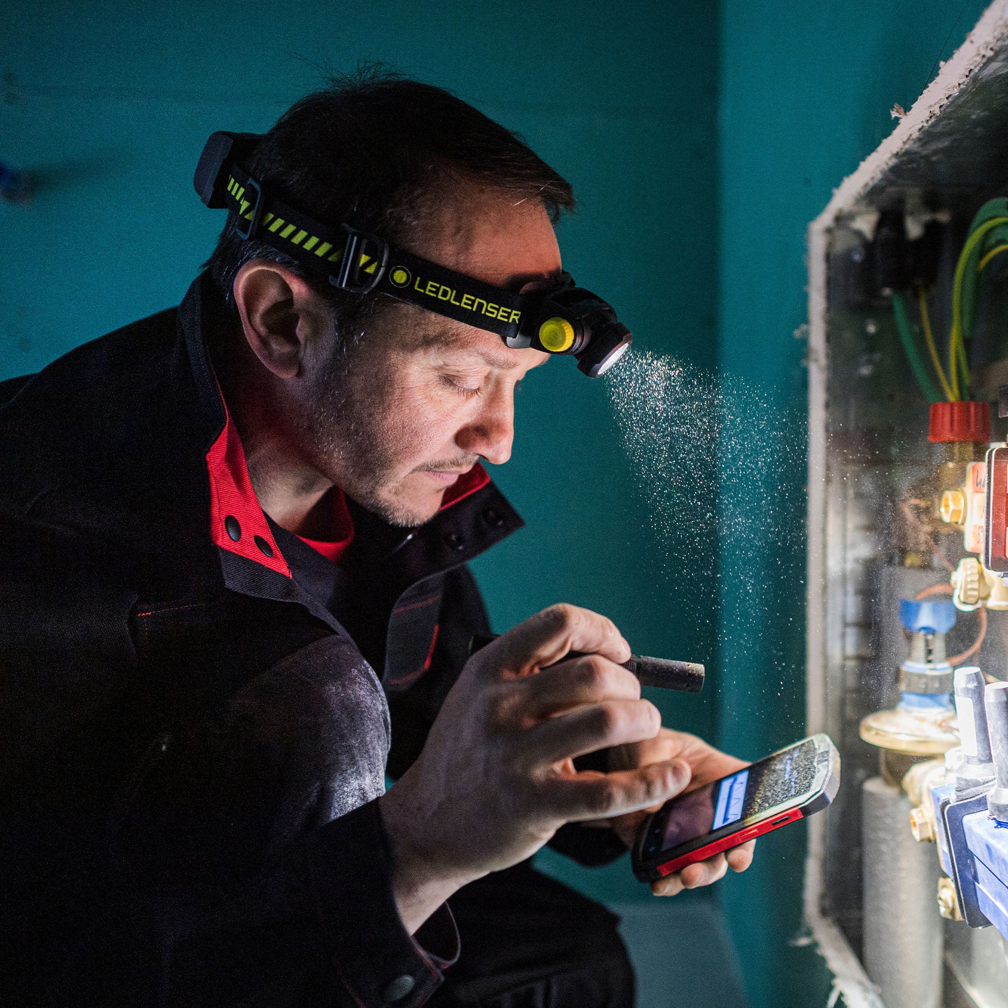 P2R Work Torch headlamp worn by a worker with a blue Ledlenser strap inspecting an electrical panel indoors