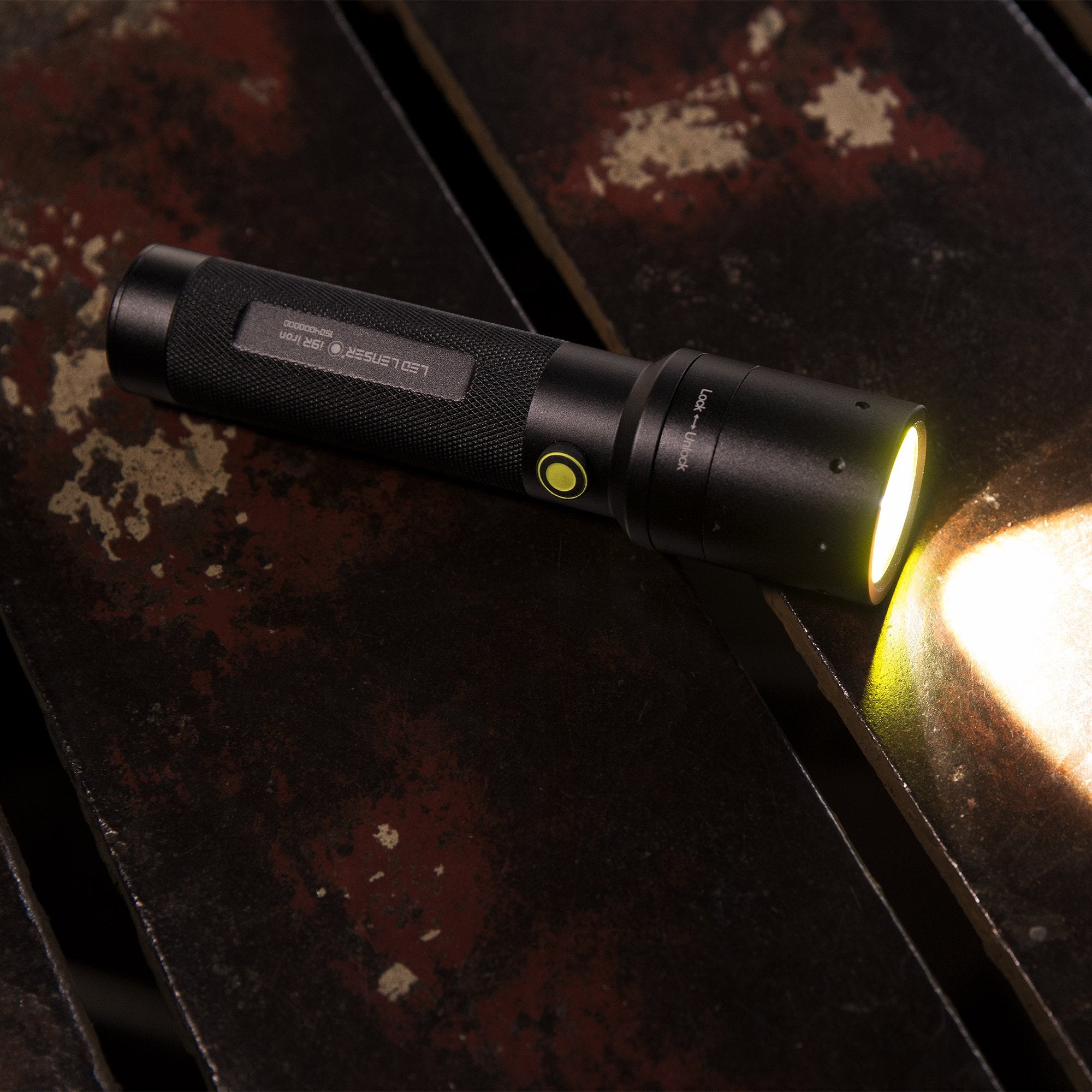 Ledlenser i9R Iron 2 rechargeable torch lying on a dark textured surface with a lit beam and yellow power button