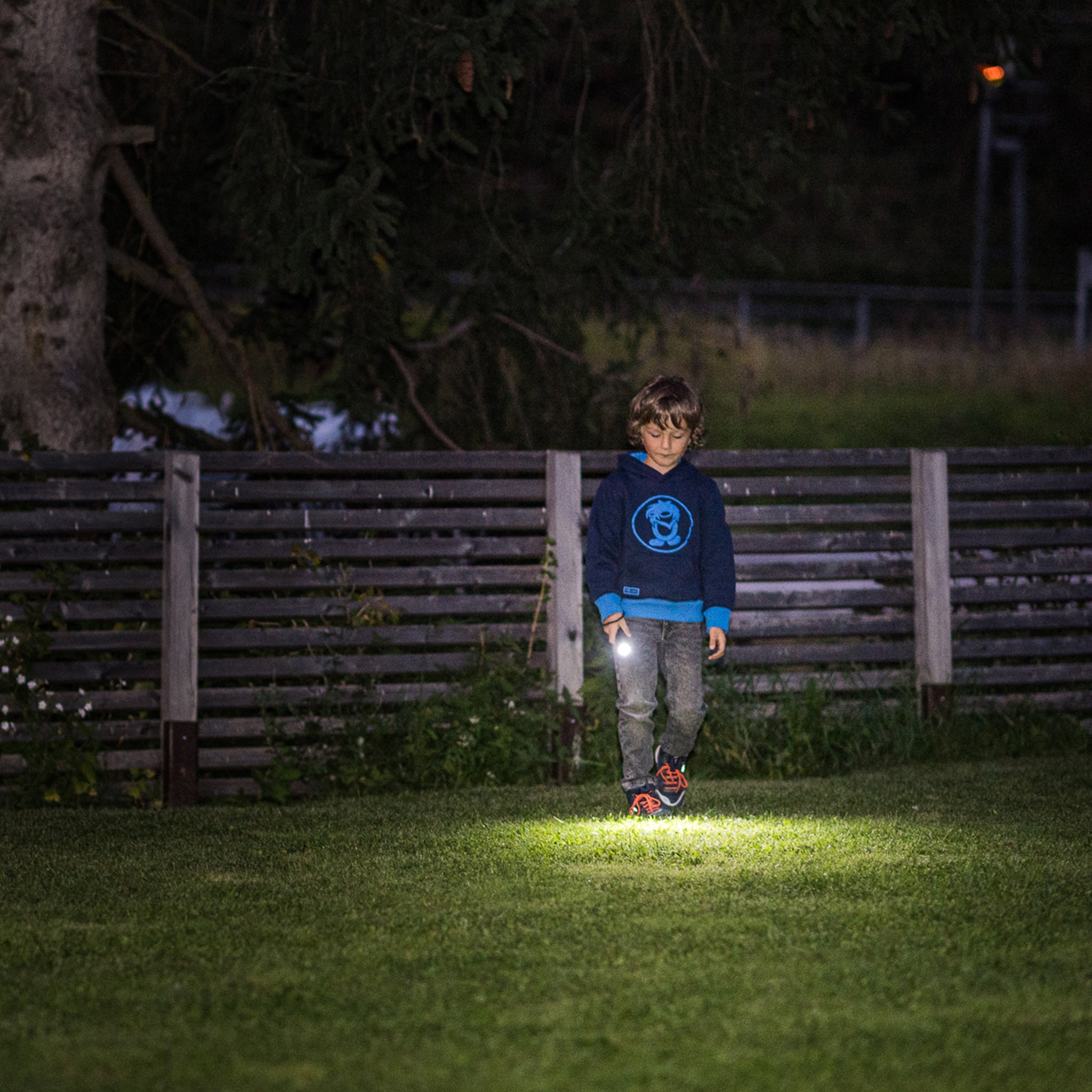 Kidbeam4 Torch battery operated children's flashlight shown held by a child in a blue hoodie at night with a bright beam on the grass