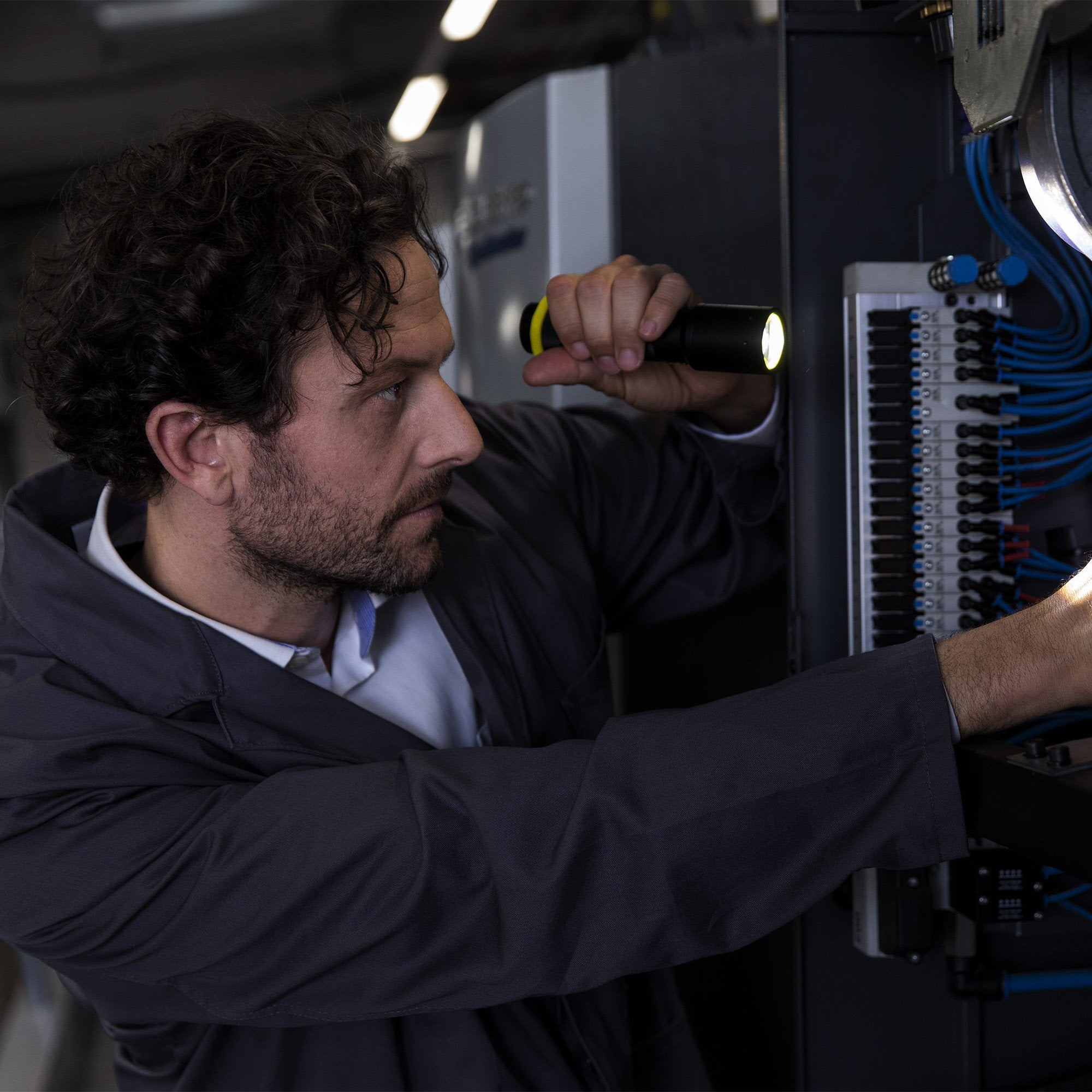 i7 Torch in black with a yellow ring held by a technician inspecting an electrical panel with wiring