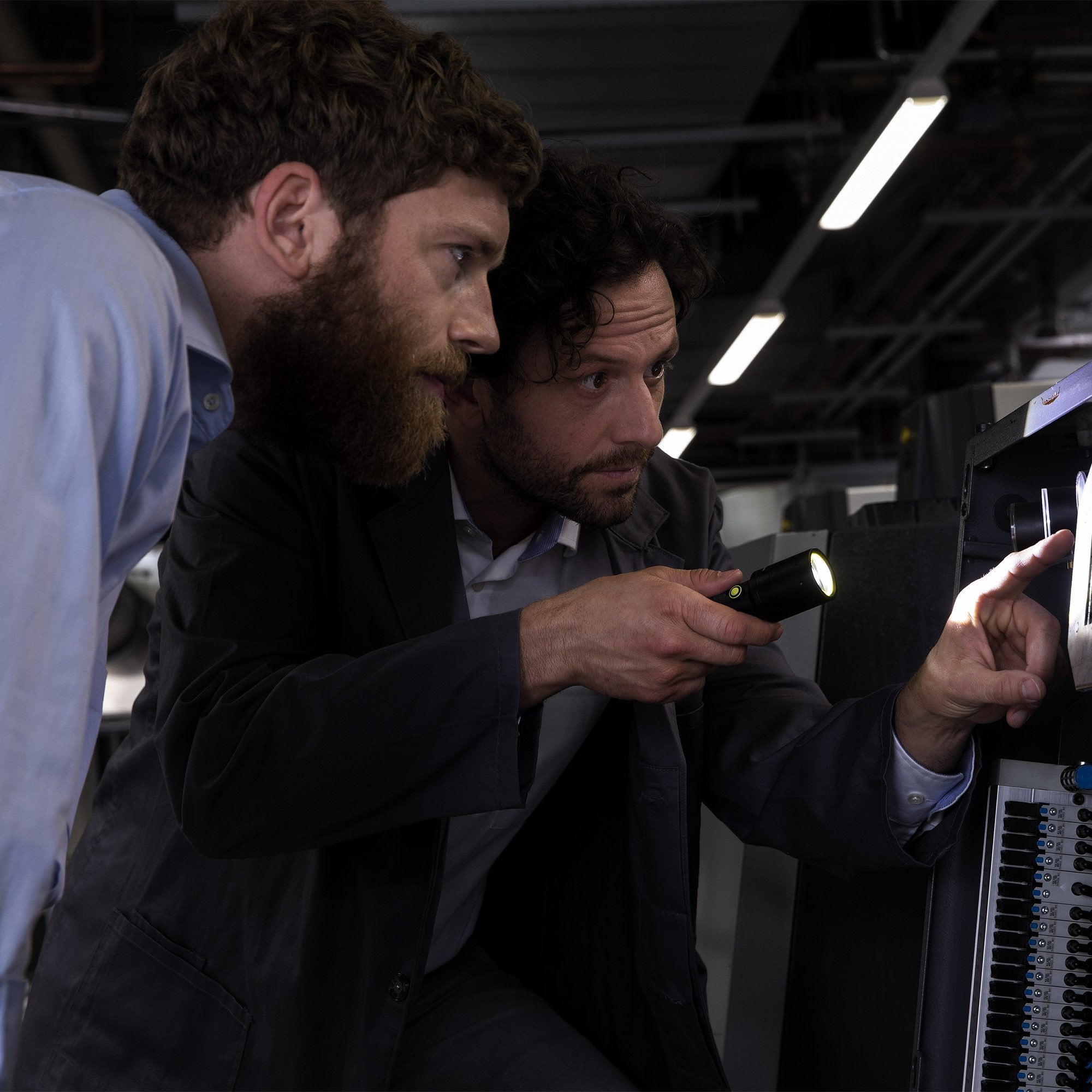 i7R Rechargeable Torch being held by a man inspecting a server rack panel with another man observing in a workshop