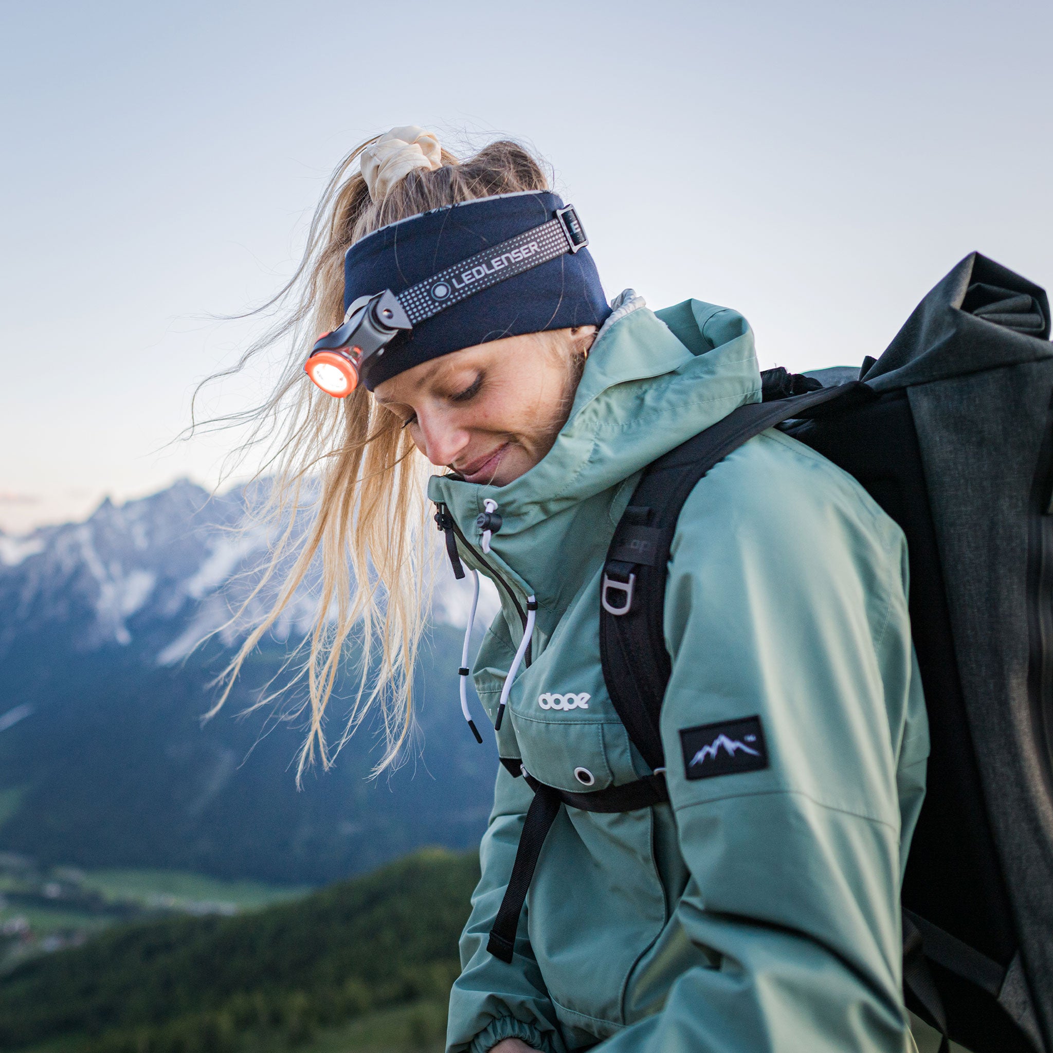 MH11 Outdoor Headlamp worn by a hiker with a blue headband and backpack red light on mountains in background