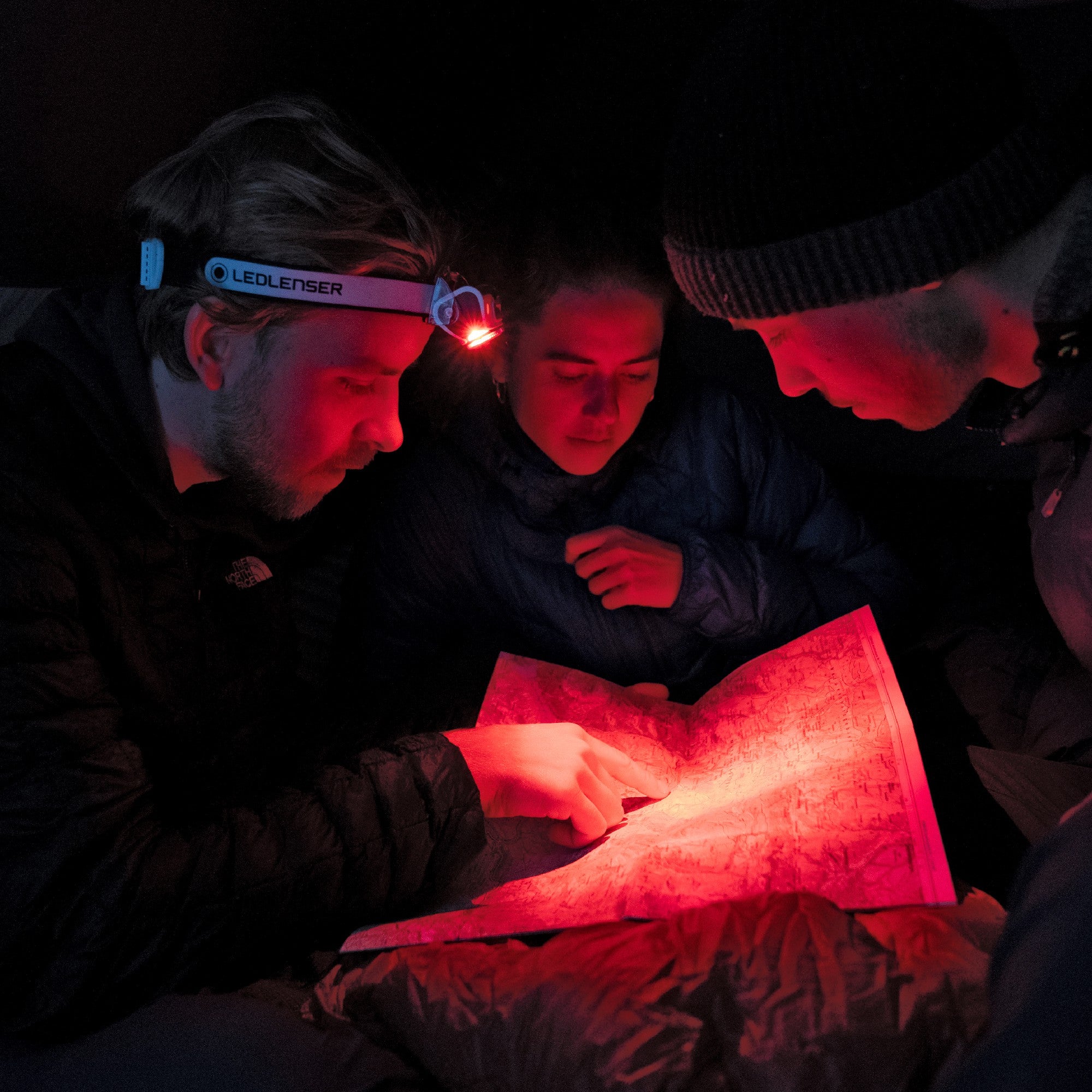 MH7 Green Rechargeable Headlamp worn by a person in a dark scene as three people study a map illuminated in red light