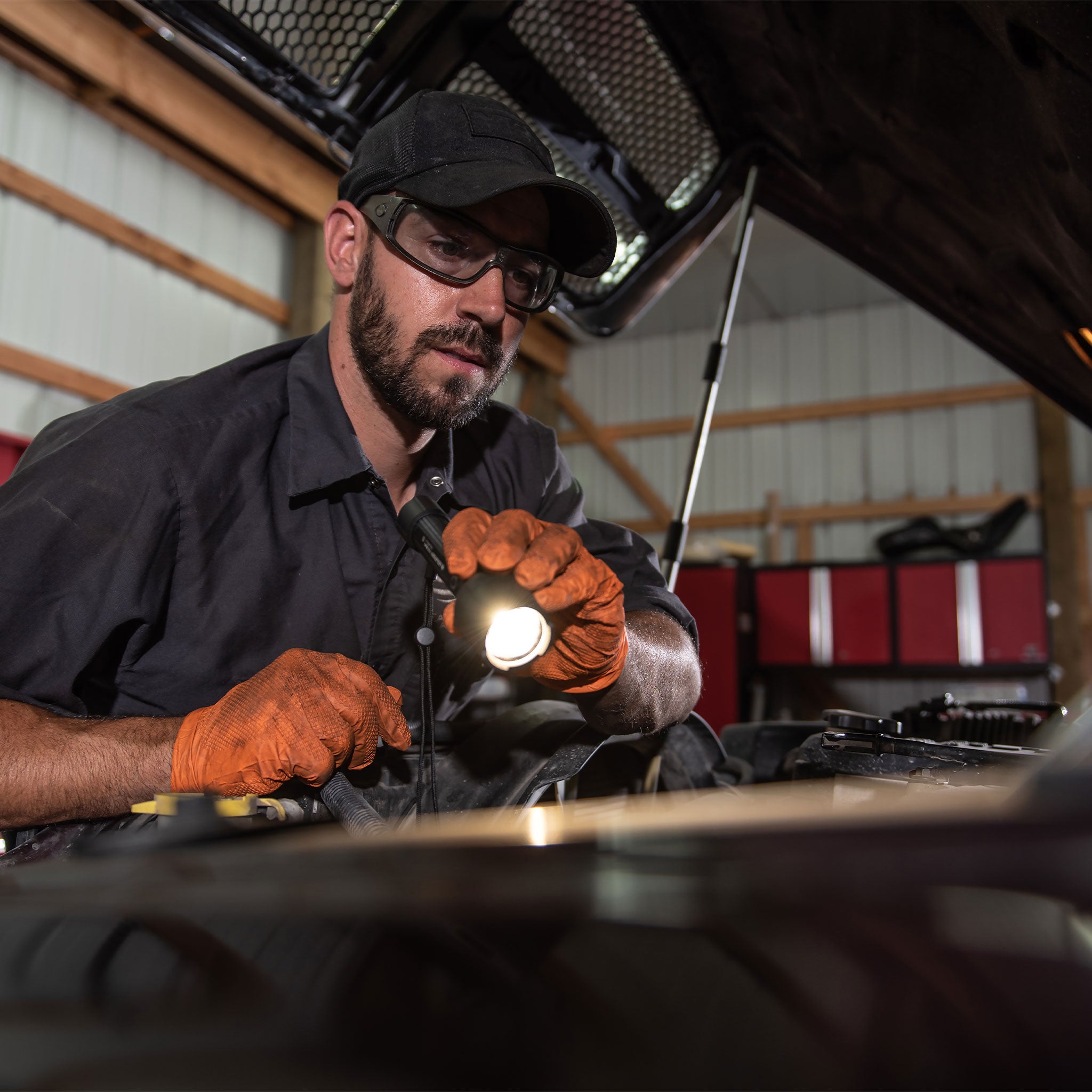 Ledlenser P6R Work Torch held by a technician wearing a cap safety glasses and orange gloves while inspecting a vehicle in a workshop