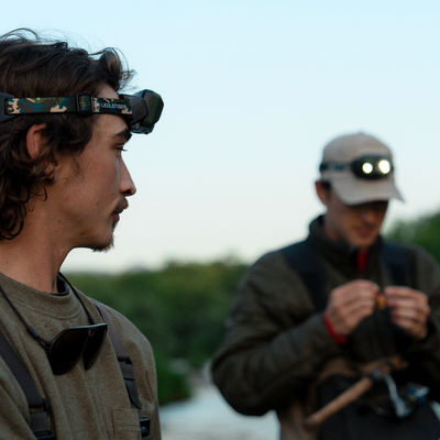 HF8R Core RGB Camo headlamp worn by a person with a camouflage headband in foreground with another lit headlamp in the background