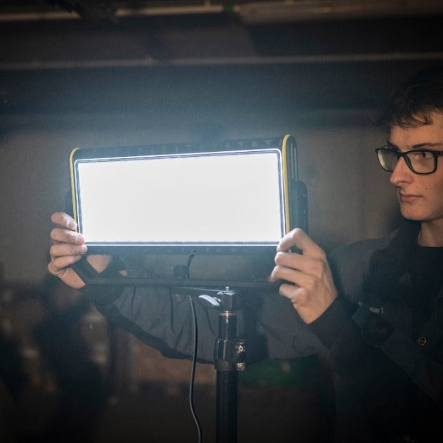 AF12C Work Floodlight held by a person in a workshop rectangular LED panel on an adjustable stand with yellow trim