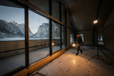 AF8R Work Floodlight with two stands in a dim industrial space man in workwear near large windows overlooking snowy mountains