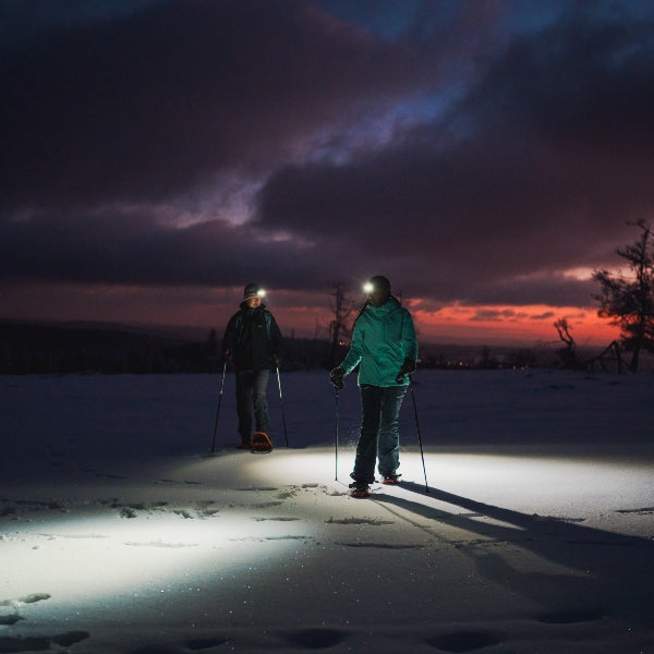 HF8R Signature Headlamp worn by hikers on a snowy dusk trail with headlamp beams illuminating the snow