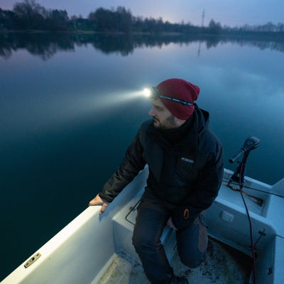 HF8R Signature Headlamp worn by a man on a boat at dusk with beam shining over calm water