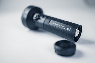 Ledlenser P18R Torch lying on its side with end cap removed exposing the internal connector and textured black body