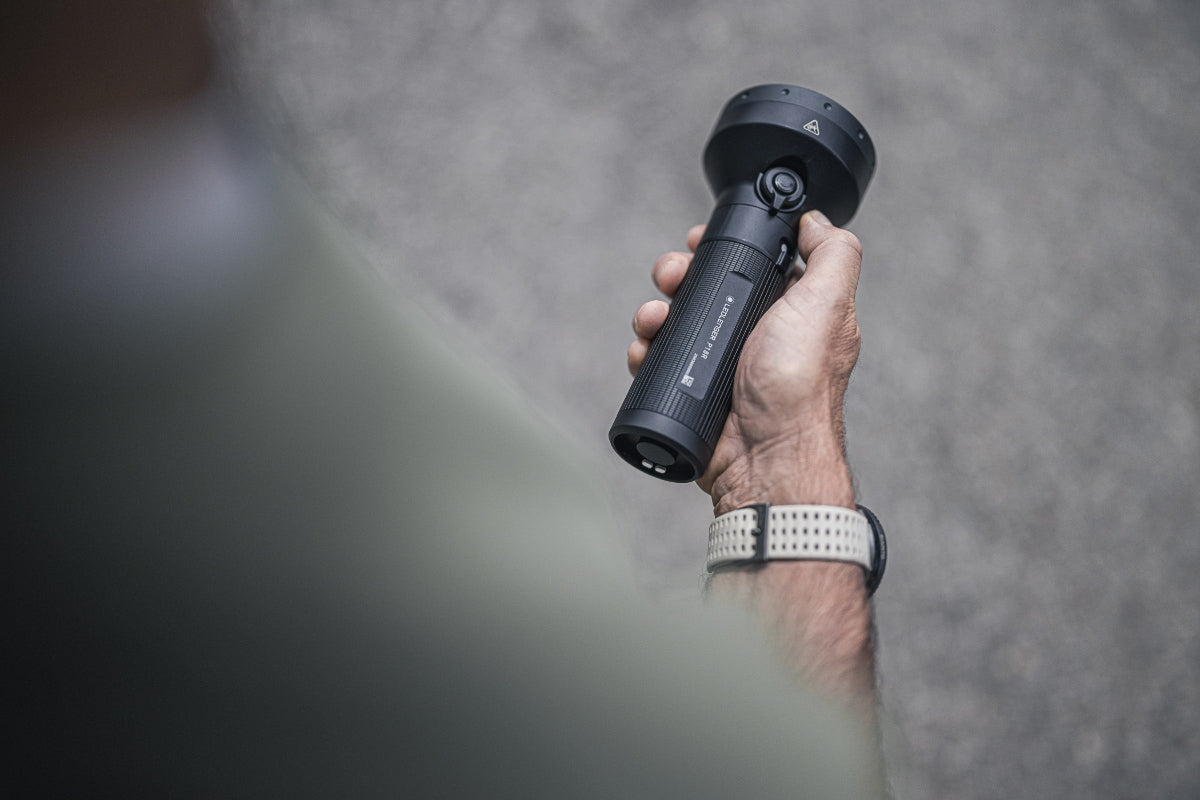 P18R Torch held in a hand black cylindrical flashlight with textured grip and large head against a grey background