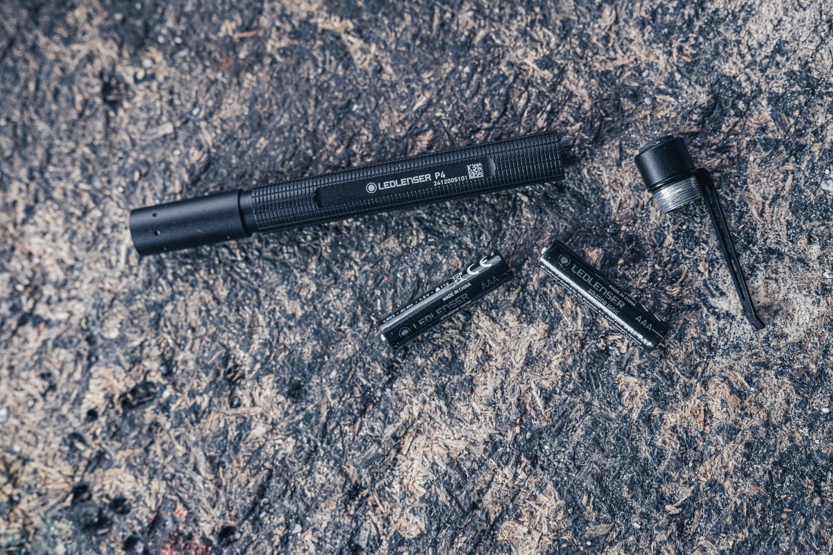 Ledlenser P4 Torch disassembled with AAA batteries and end cap shown as a compact black flashlight on a rocky surface