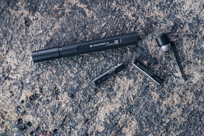 Ledlenser P4 Torch disassembled with AAA batteries and end cap shown as a compact black flashlight on a rocky surface