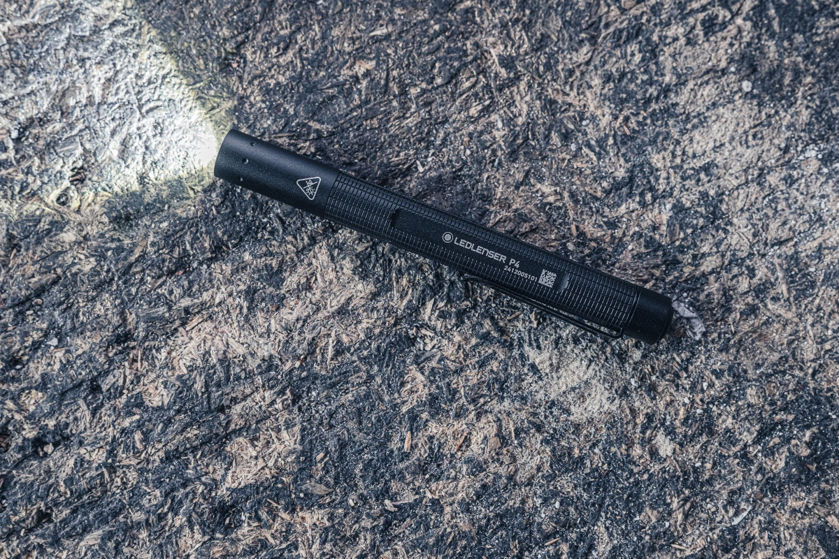 Ledlenser P4 Torch lying on a rocky surface; black compact flashlight with textured grip and a visible beam