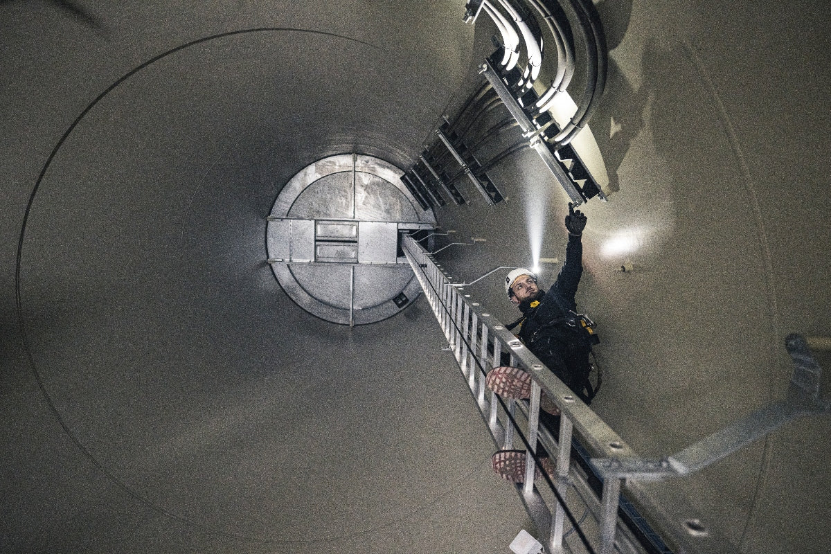 Ledlenser P5R Pro Torch used by a worker in helmet inside an industrial vertical shaft standing on a metal ladder and reaching with a handheld light