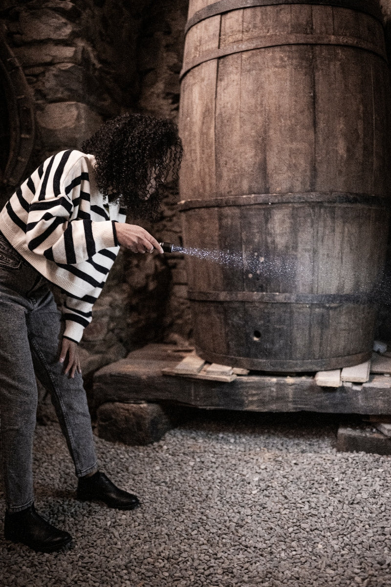 P5R Torch held by person in a striped sweater spraying mist toward a large wooden barrel in a rustic setting