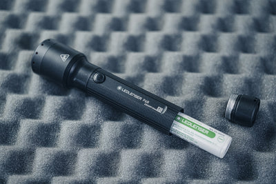 P6R Torch lying on foam backdrop with battery and cap nearby; a black Ledlenser torch with textured grip and side button
