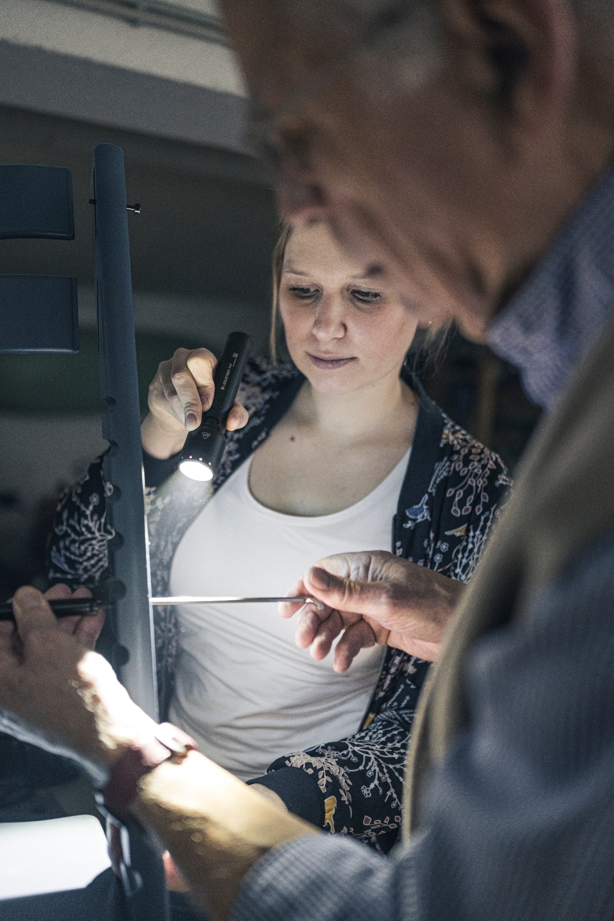 Ledlenser P6R Torch handheld flashlight in use during a workshop task with a second person assisting nearby black finish